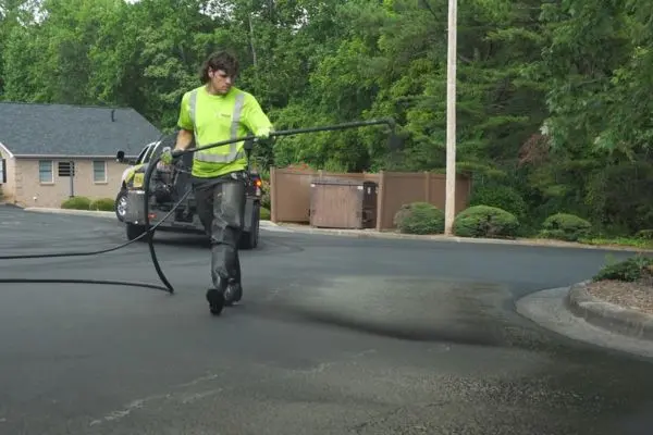Person applying spray coat on pavement.